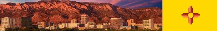 Buildings surrounded by large mountains with the state flag of New Mexico.
